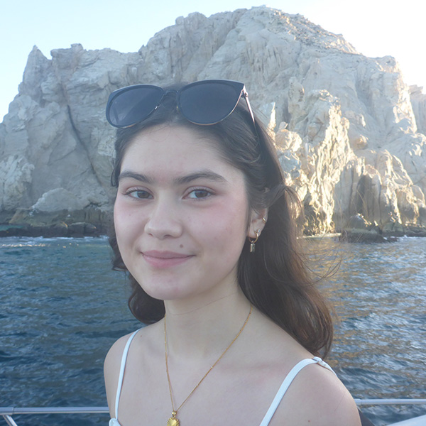 Amelia smiling for the camera with the ocean and large rock formations in the background