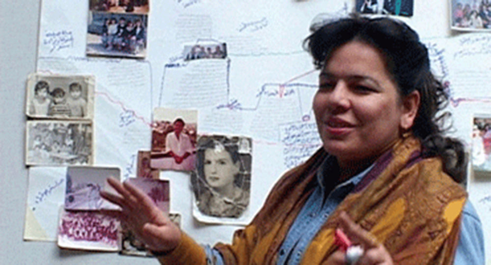 A woman stands in front of a board covered with photos and letters