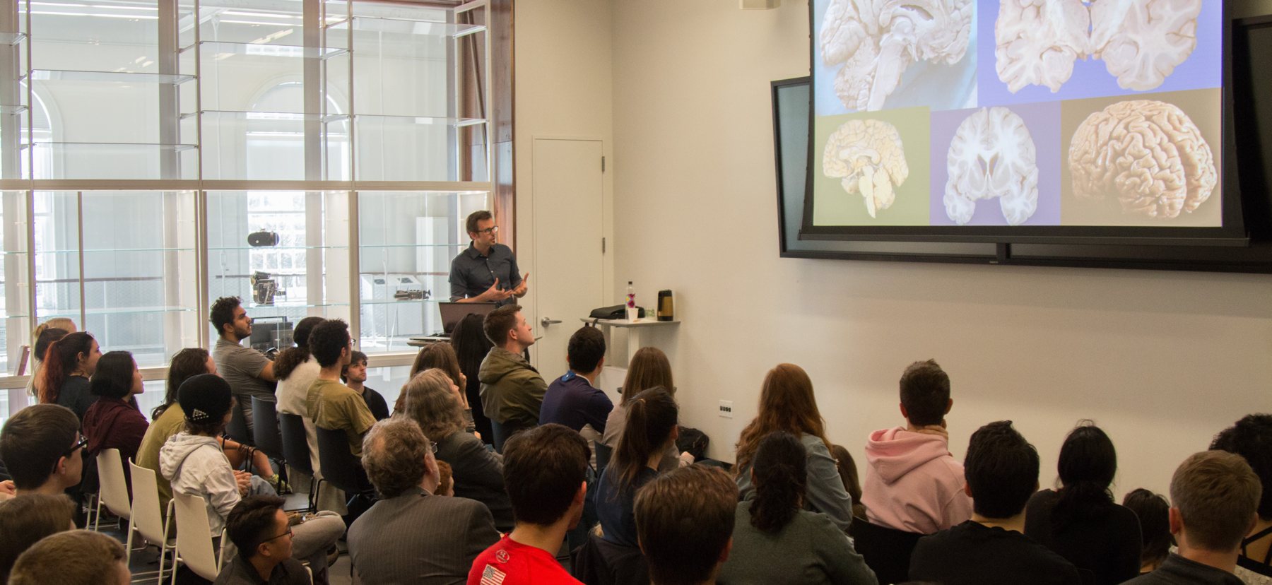 A man displays speaks in front of a class about a presentation of the human brain