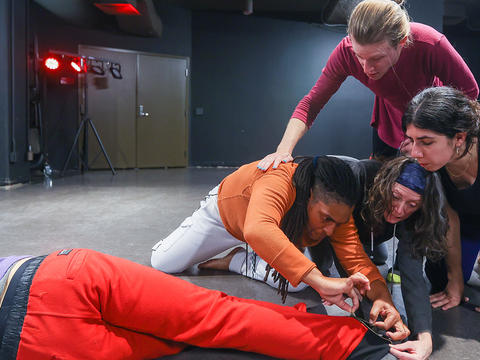 Several performers huddle around another who is lying on the floor of the black box theater in Haverford's dining center. 