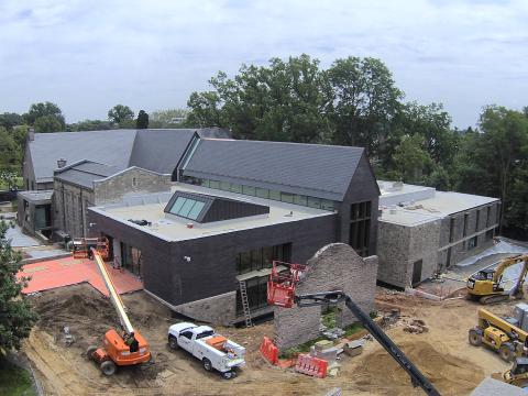 Exterior of the library under construction on a sunny day, with cherry picker machines in the foreground.