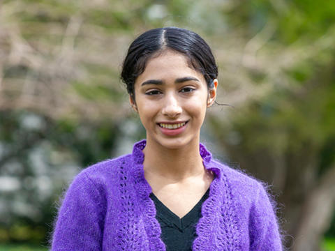 Aamina Dhar smiling for the camera in a purple sweater against a soft focus background of Haverford college foliage