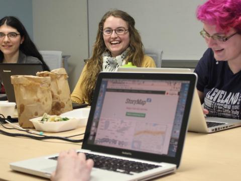 a group of student workers at a table, working at laptops and eating lunch