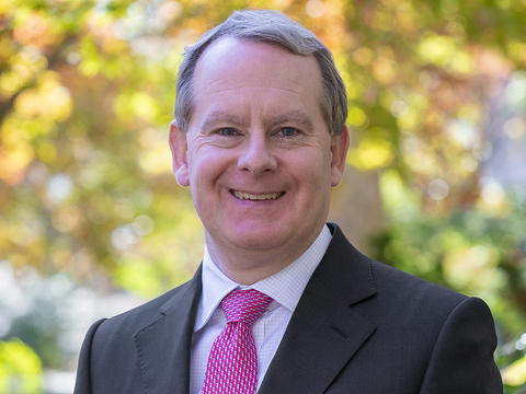 Alex Robinson is pictured in a portrait on Haverford's campus. He wears a light shirt, red patterned tie, and dark suit jacket.