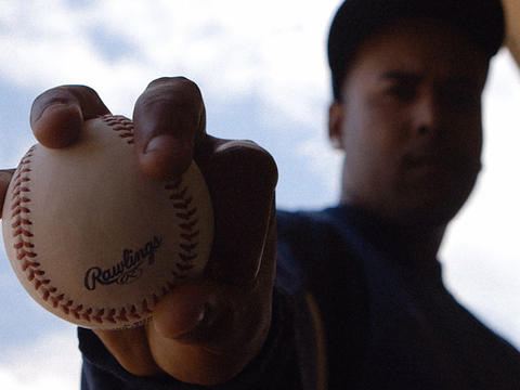 A baseball player holds a ball up to the camera in a still from a documentary. 