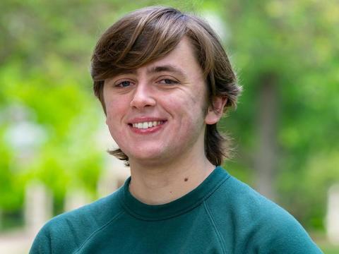 Charlie Crawford smiling for the camera in a teal shirt against a soft focus background of foliage