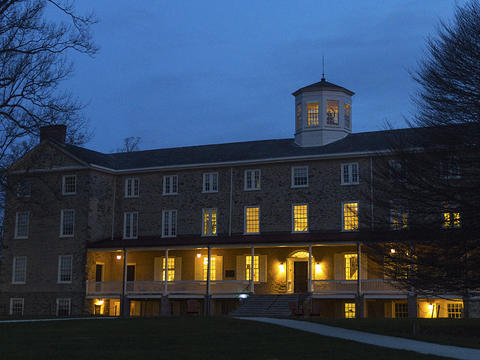 An illuminated Founders Hall is pictured against a blue sky at sunrise.
