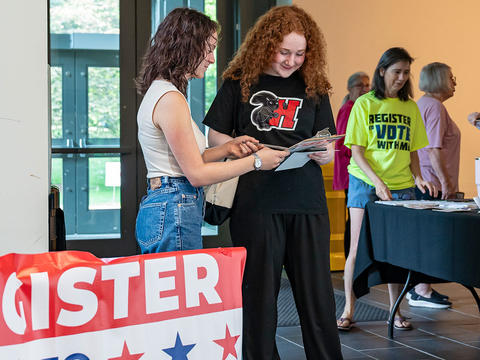 Two students look at a clipboard as they register to vote in the GIAC. One is wearing a black Haverford t-shirt with the black squirrel on it. 