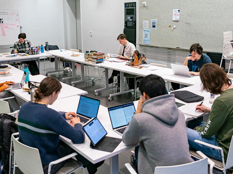 Students work on their finals while seated at tables forming a large rectangle.