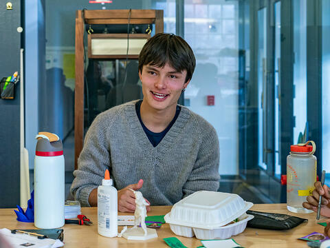 Emile Roth wears a grey sweater as he sits surrounded by students in Haverford's Maker Arts Space. 