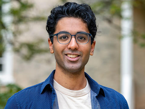 Vivek Veluvali is pictured in a portrait on Haverford's campus. He wears a blue shirt and dark glasses. 