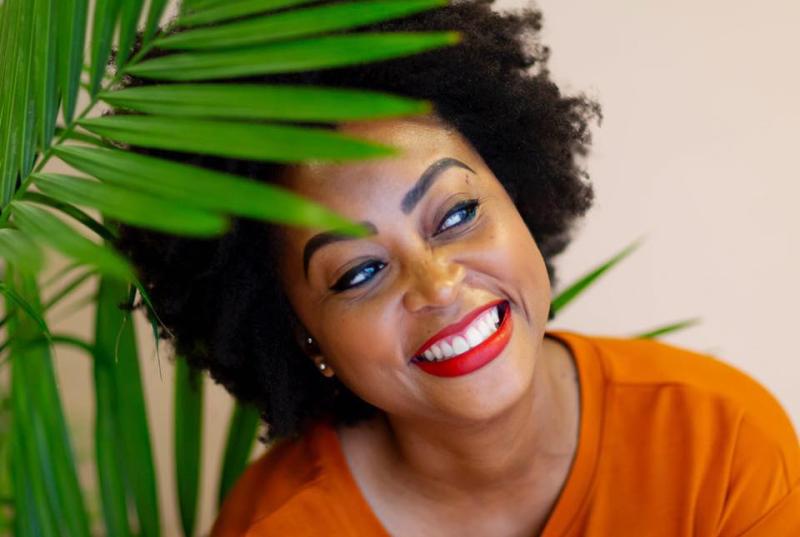 Close shot of woman smiling looking to her left in orange shirt in front of a plant
