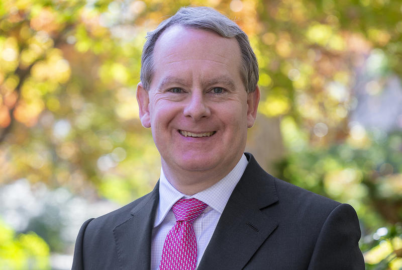 Alex Robinson is pictured in a portrait on Haverford's campus. He wears a light shirt, red patterned tie, and dark suit jacket.