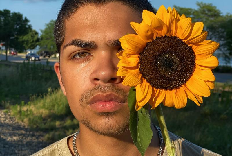 Kevin holds a large, yellow sunflower in front of his left eye
