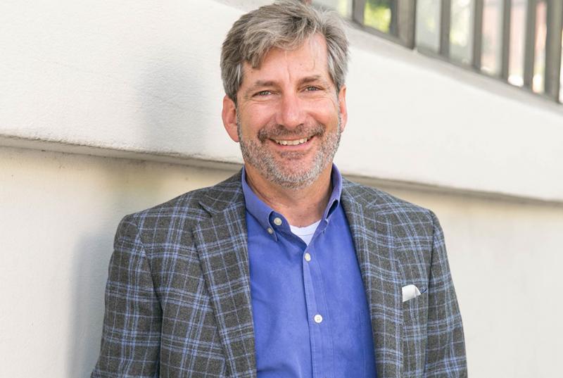 A portrait of Mark Miller '84, wearing a blue shirt and a gray and blue checked blazer