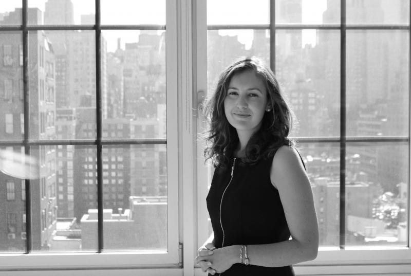 A black and white portrait of Sarah Astheimer '01, standing in front of large windows overlooking Manhattan