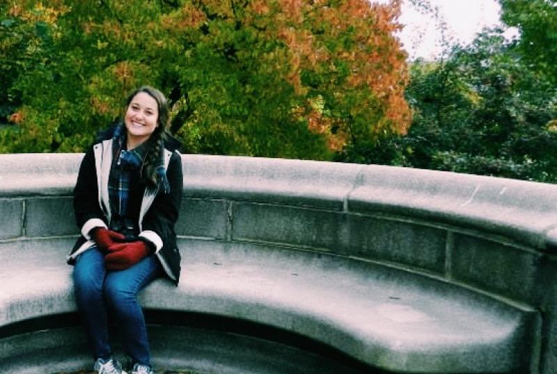 Kristen Andersen sitting on a stone bench in front of fall foliage