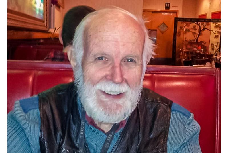 Daniel Gillis smiles through his white beard while sitting in a red vinyl restaurant booth