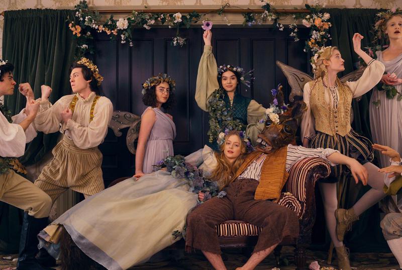 The cast of Dickinson in period costume, draped in flowers, during an onscreen performance of "A Midsummer Night's Dream" with one of the actors in a donkey mask