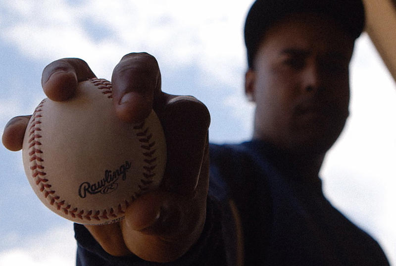 A baseball player holds a ball up to the camera in a still from a documentary. 