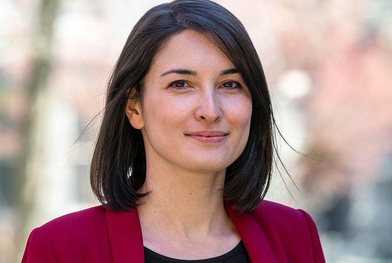 Emily Hong is pictured against a blurry background. She wears a red blazer with a black shirt beneath.