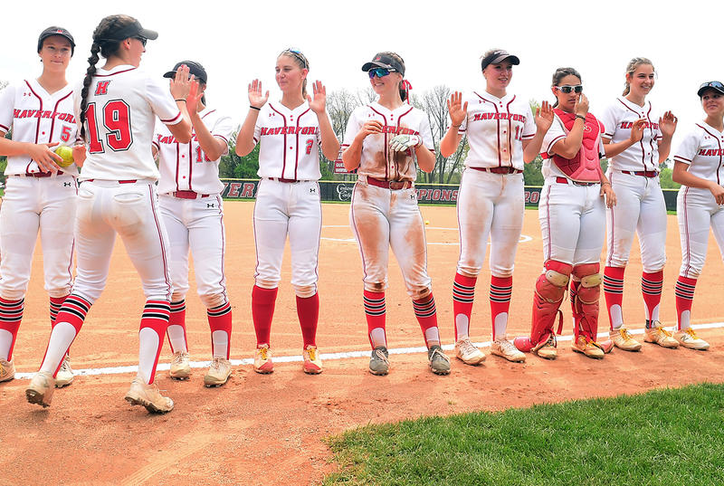 Members of Haverford's softball team line up for high fives while wearing white uniforms with red socks.