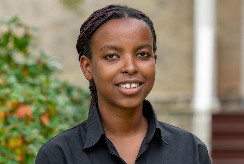 Ghislaine Niyodusenga looks at the camera in a portrait. She wears a black button up shirt and is pictured in front of a building on Haverford's campus. 