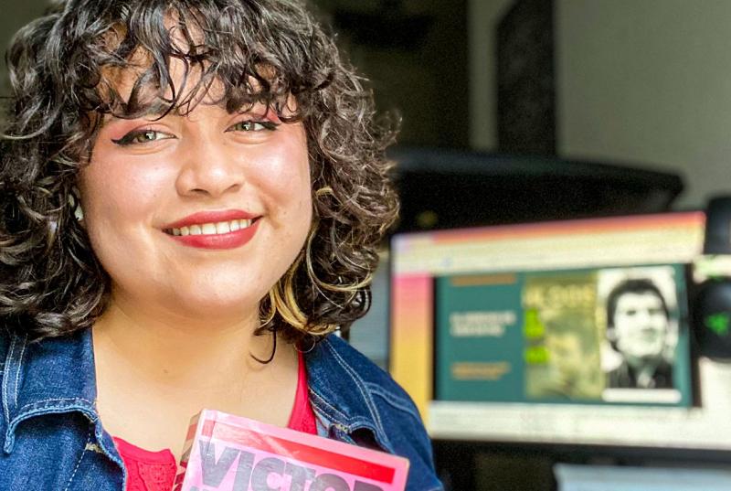 A picture of Lía holding up a book with a computer monitor in the background.