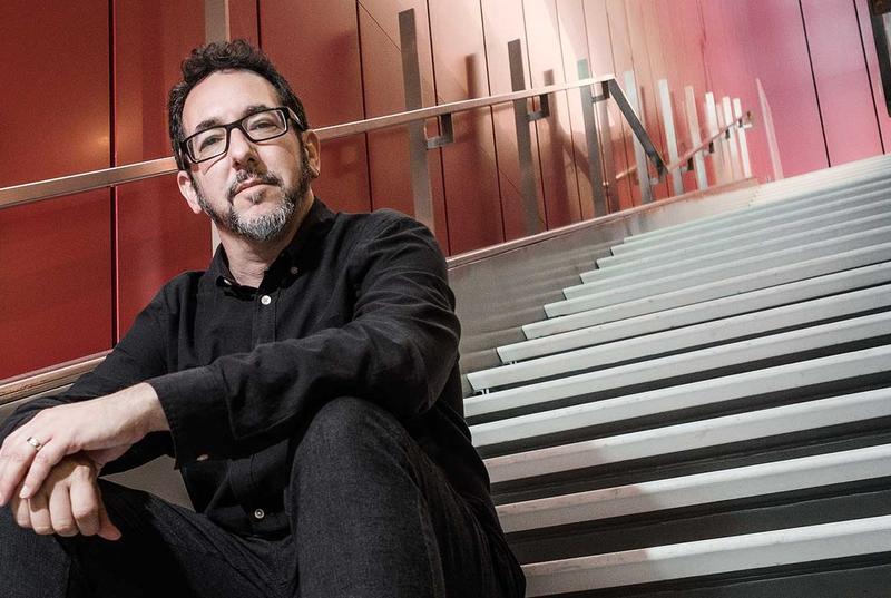 Photo of Bill Bragin, dressed in a black shirt and black pants, sitting on stairs