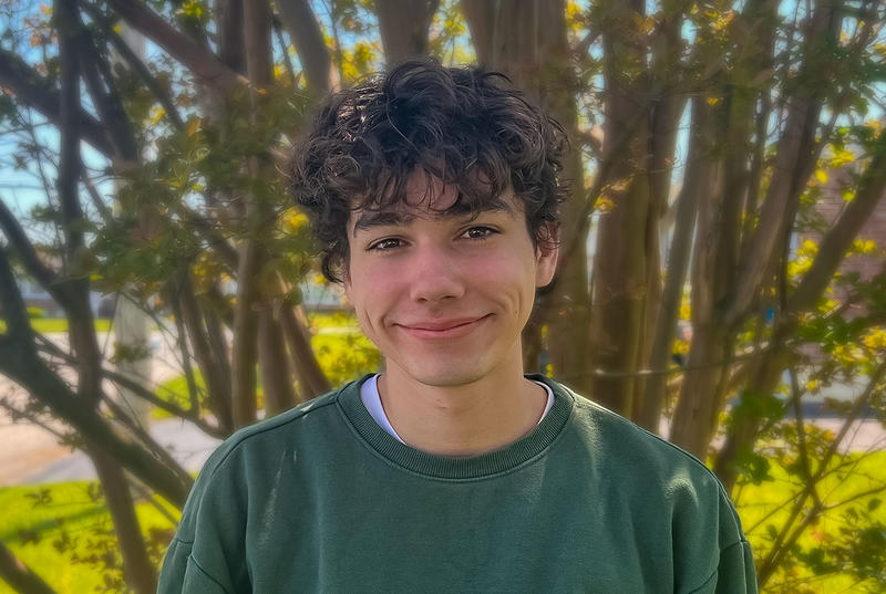 Patrick Kelly wears a green sweater and is pictured against an out-of-focus background.