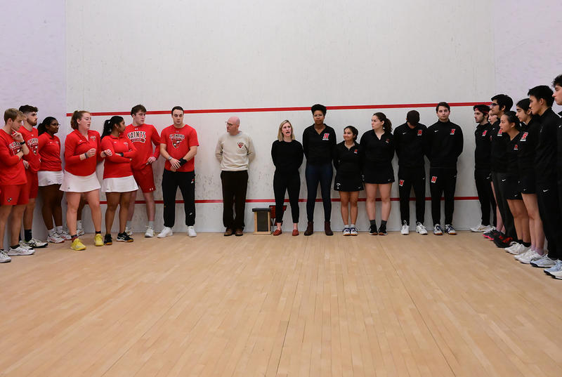Members of the men's and women's squash teams line the walls of Haverford's court wearing the College's colors. 