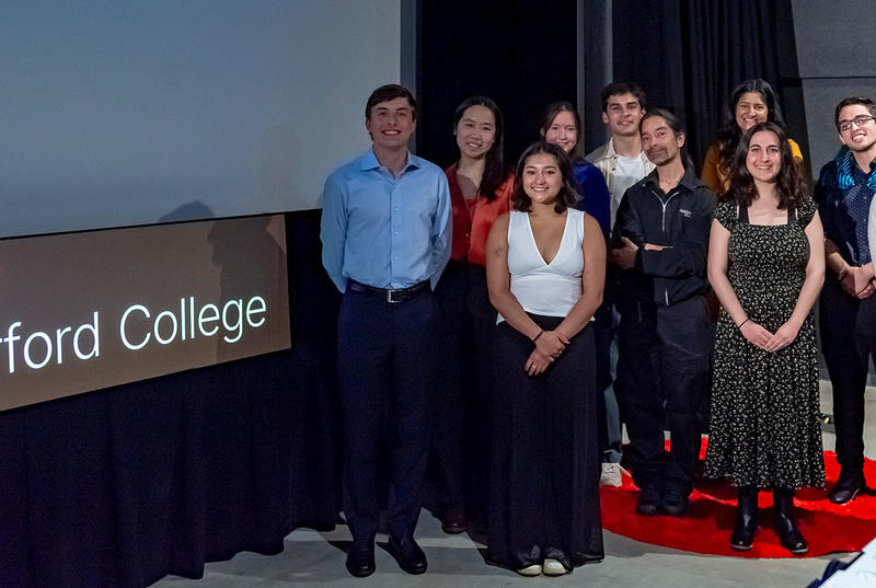 A group of 10, comprising Haverford students, staff and faculty, stand in front of a screen and a sign that reads TEDx Haverford College