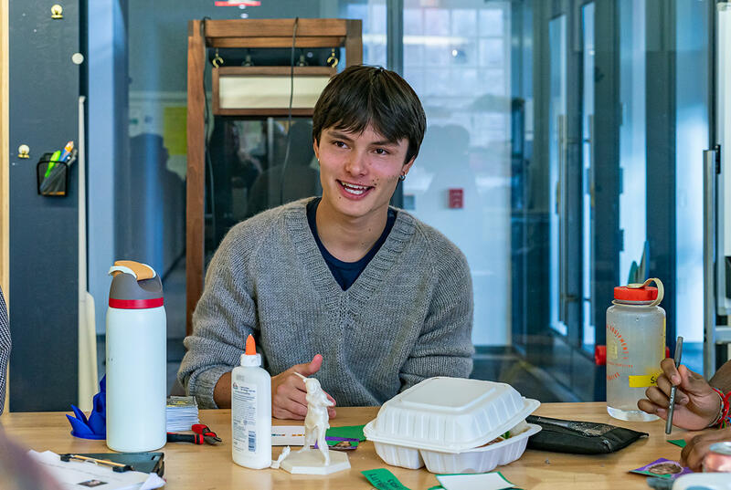 Emile Roth wears a grey sweater as he sits surrounded by students in Haverford's Maker Arts Space. 