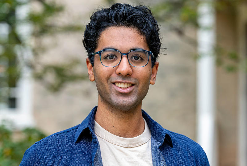 Vivek Veluvali is pictured in a portrait on Haverford's campus. He wears a blue shirt and dark glasses. 