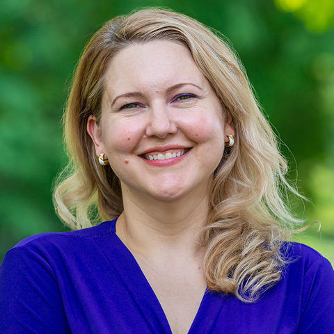 Headshot of Lora Lowe smiling for the camera against a soft focus background of Haverford College foliage