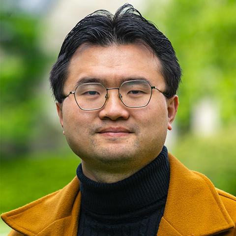 Leslie Shi in a ochre colored blazer and dark blue turtleneck against a soft-focus nature background.
