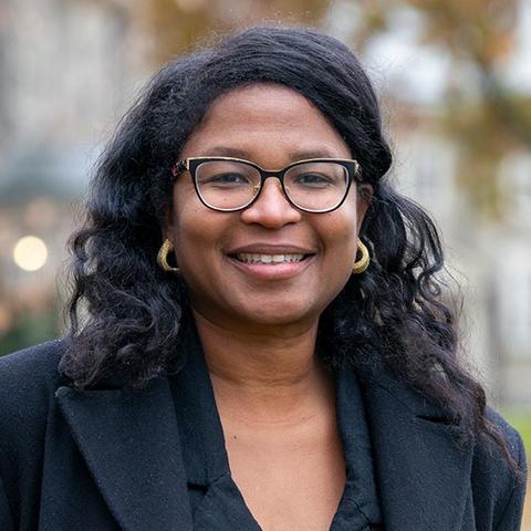 Ronah Harris in glasses and a black blazer smiling for the camera