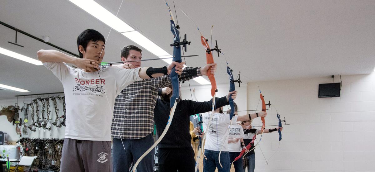 Students in a line with arrows nocked in compound bows
