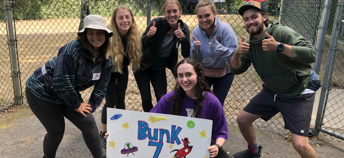 Photo of Isabel Russak at the bottom holding a "Bunk 7" sign with her co-counselors around her.