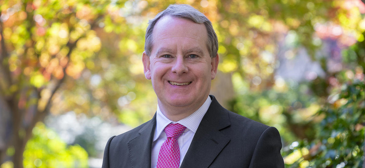 Alex Robinson is pictured in a portrait on Haverford's campus. He wears a light shirt, red patterned tie, and dark suit jacket.