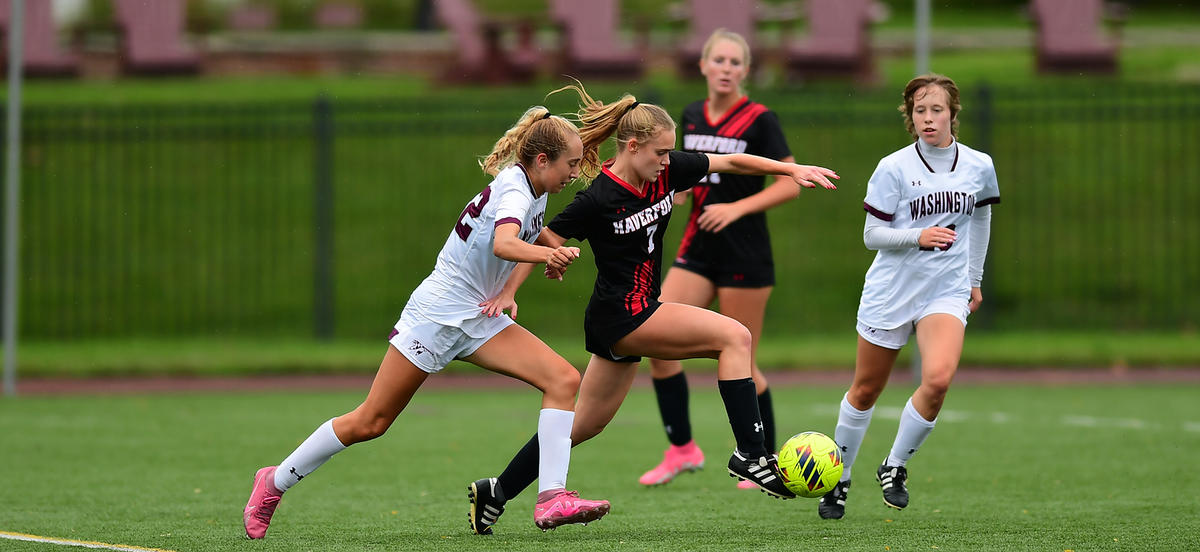 Olivia D'Aulerio, wearing a black and red Haverford soccer uniform, dribbles past a defender during a fall soccer match. 