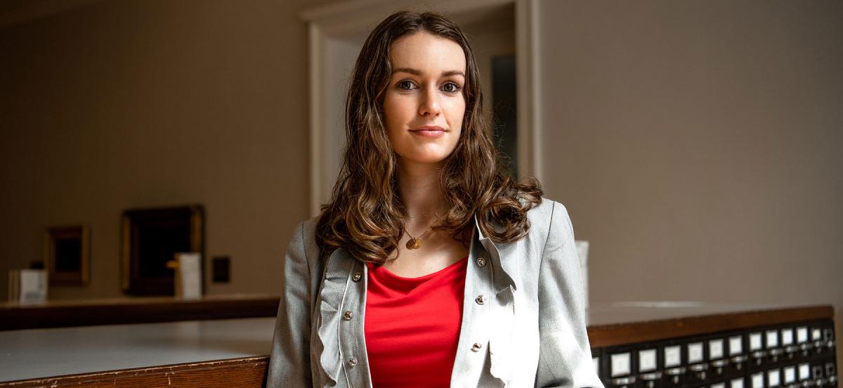 Headshot of Becca wearing a black shirt and grey jacket in the archive.