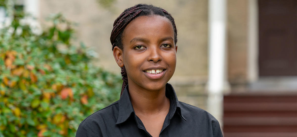 Ghislaine Niyodusenga looks at the camera in a portrait. She wears a black button up shirt and is pictured in front of a building on Haverford's campus. 