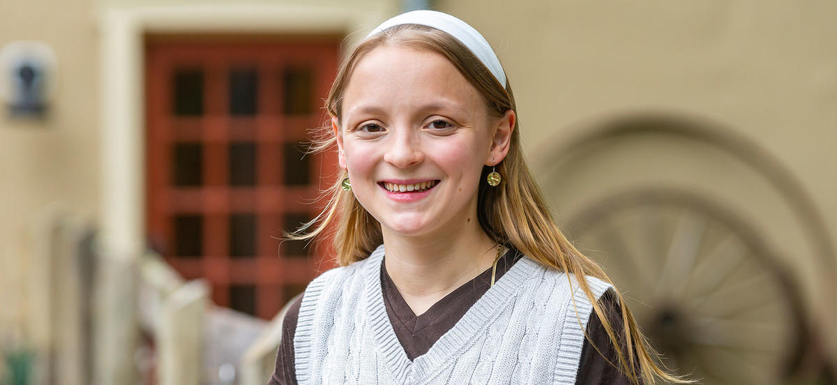 Isabella Otterbein is pictured in a portrait wearing a white headband and a white sweater over a dark-colored shirt. 