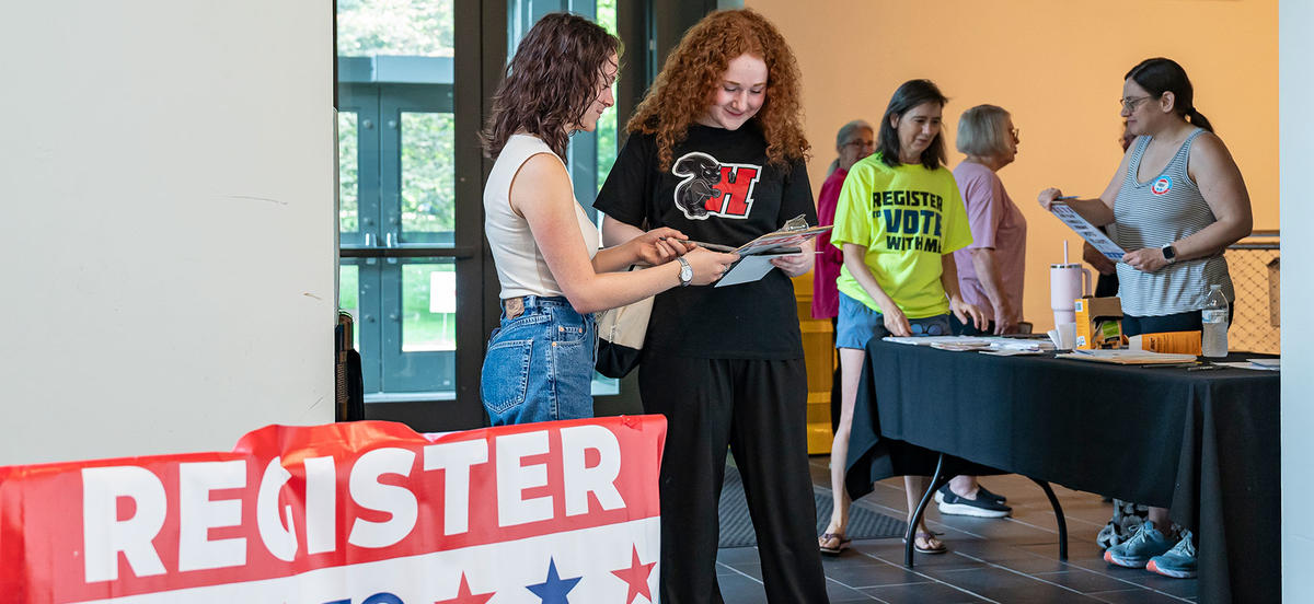 Two students look at a clipboard as they register to vote in the GIAC. One is wearing a black Haverford t-shirt with the black squirrel on it. 