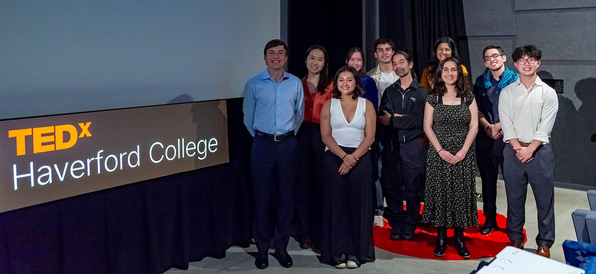 A group of 10, comprising Haverford students, staff and faculty, stand in front of a screen and a sign that reads TEDx Haverford College