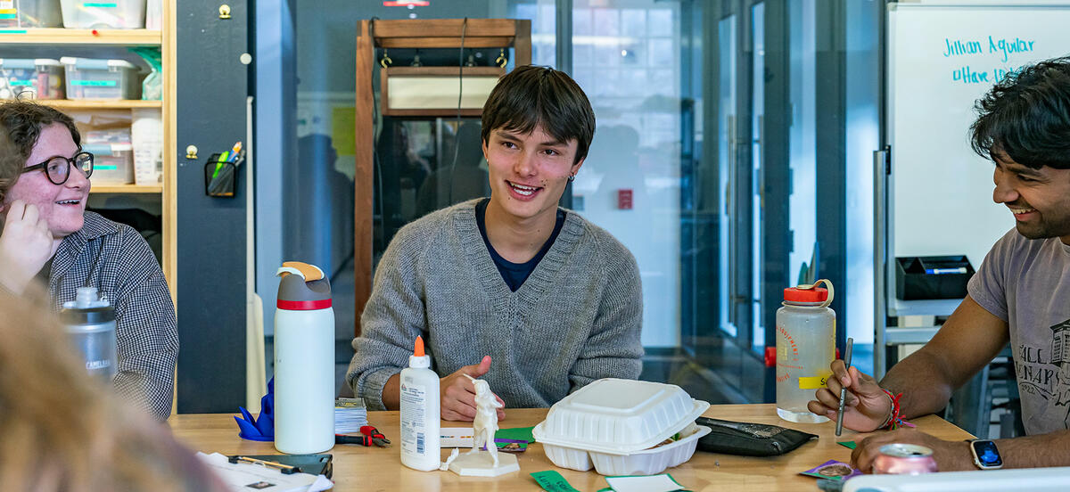 Emile Roth wears a grey sweater as he sits surrounded by students in Haverford's Maker Arts Space. 