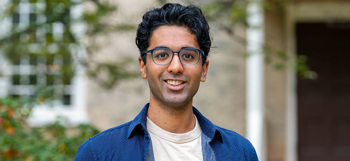 Vivek Veluvali is pictured in a portrait on Haverford's campus. He wears a blue shirt and dark glasses. 