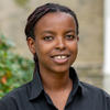 Ghislaine Niyodusenga looks at the camera in a portrait. She wears a black button up shirt and is pictured in front of a building on Haverford's campus. 