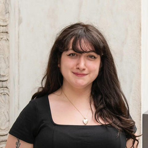 Headshot of Sarah Weill-Jones. Sarah has long brown hair, and bangs. Sarah is a feminine presenting person wearing a black top.